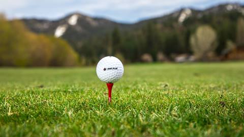 A Bear Mountain Golf Course branded golf ball teed up on a red tee that is teed up on the grass.