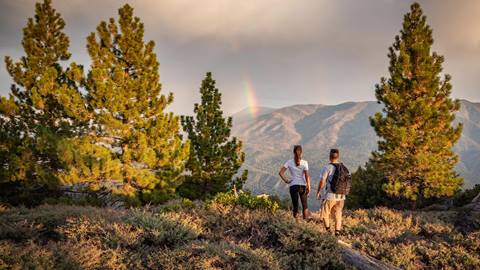 A couple hiking and enjoying the view of a rainbow.