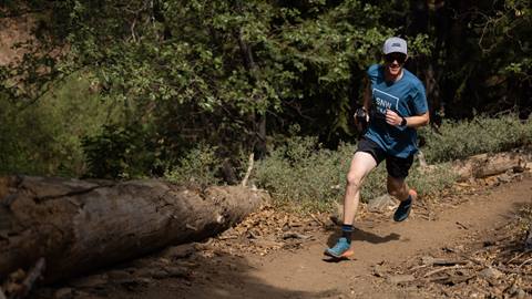 male wearing a blue snow summit shirt and a grey hat running on a dirt trail