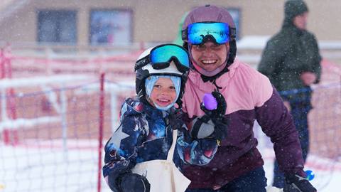 An adult with their kiddo, in snow gear during a snow storm, who is holding a purple easter egg at Snow Valley