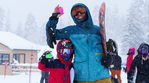 Adult in blue snow jacket holding a snowboard with kiddo in red jacket holding up their easter egg finds from the scavenger hunt