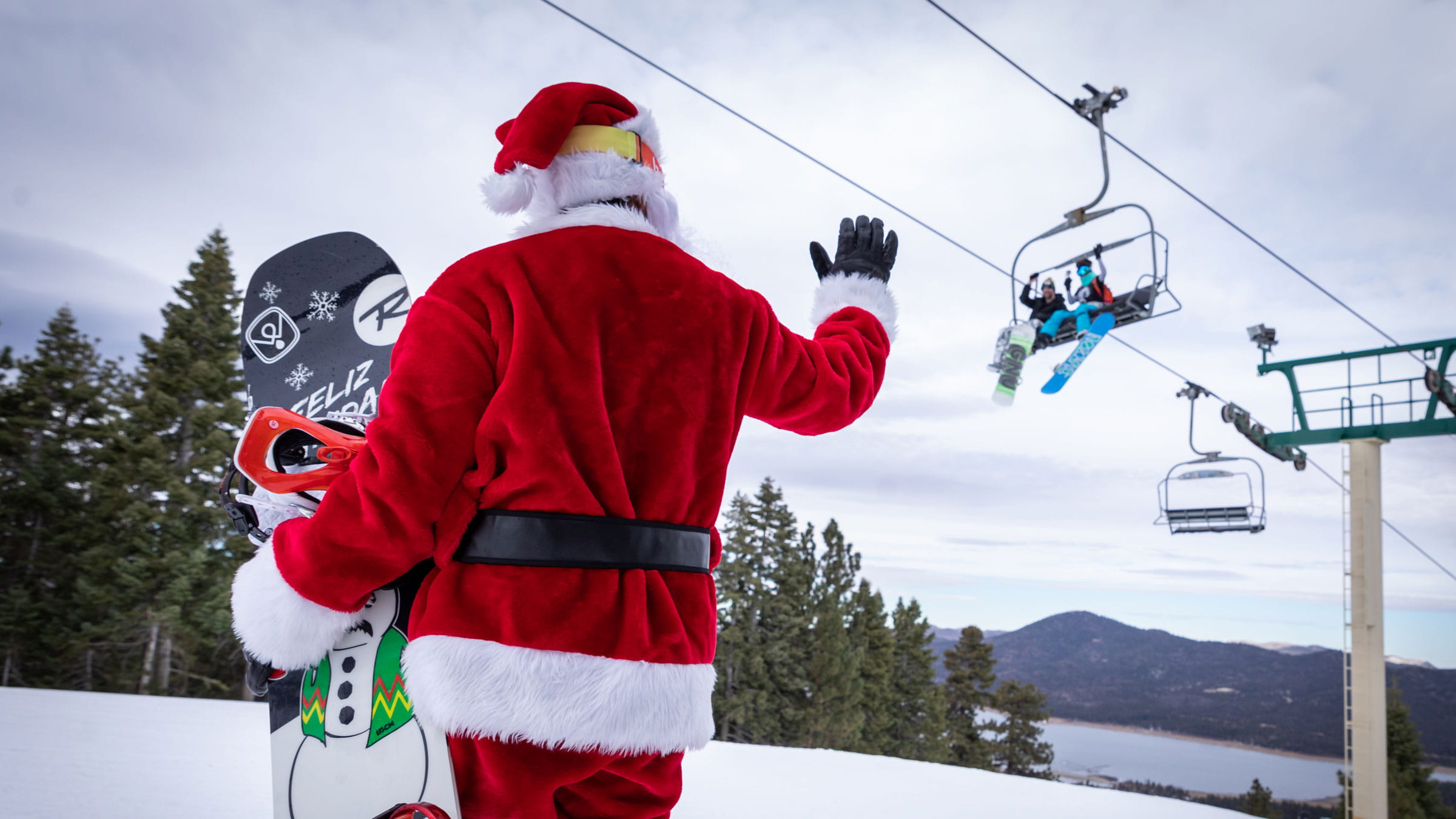 Santa waving at snowboarders on a chairlift