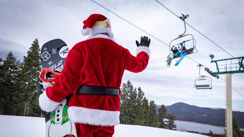 Santa waving at snowboarders on a chairlift