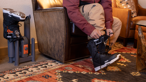 snowboarder sitting on a chair and putting on his snowboarding boots in the Ikon Pass Suite at Snow Summit