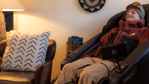 snowboarder sitting in a massage chair in the Ikon Pass Suite at Snow Summit