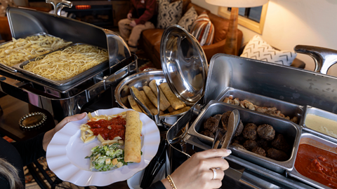catered food displayed on a table with a hand grabbing food in the Ikon Pass Suite