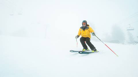 Skier in yellow jacket riding through new snow and fog during a snow day at Snow Valley