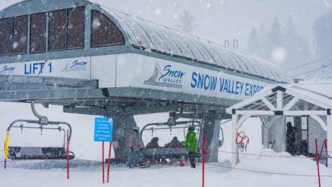 A close up of a Snow Valley employee, in a green snow jacket, loading skier and snowboarders onto the chairlift during a winter storm day.