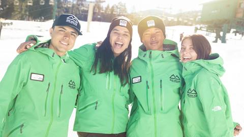 Employees at Snow Summit wearing green jackets, standing outside on the snow in big bear, posing for a photo