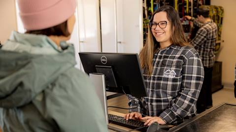 A female rental shop team member helping a guest out to pick her ski rentals