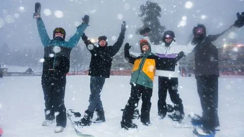 Five snowboarders with hands in air enjoying fresh snowfall