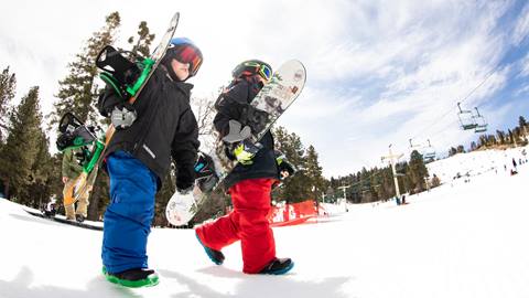 Two kid snowboarders carrying their snowboards