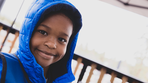 Close up of kid smiling, wearing a blue hoodie jacket and pulled hoodie to cover head