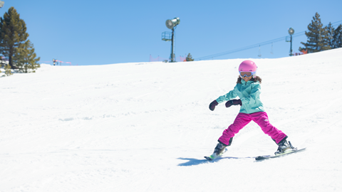 Child on skis going downhill, wearing pink snow pants and helmet, and a teal snow jacket.