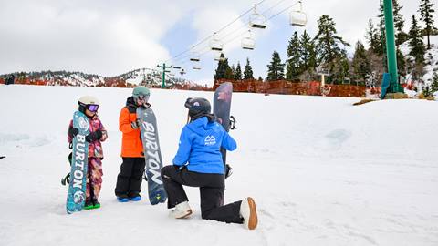 Two kiddo snowboarders with a Big Bear Mountain Resort snowboard instructor standing at the bottom of the hill.