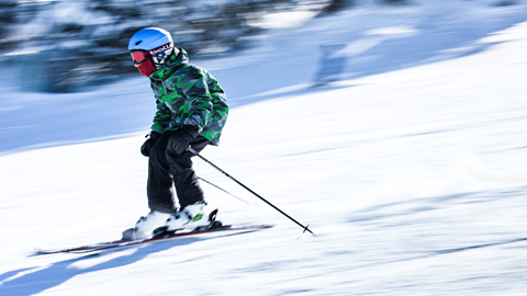 Child going downhills on skis, background blurry due to fast speed