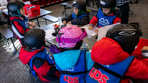 kids wearing snowboard and ski gear sitting at a table coloring