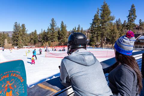 parents watching their kid take a ski lesson