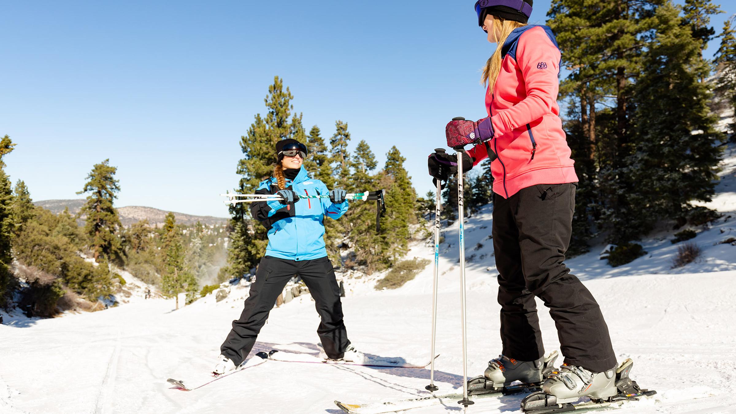 Skier in a pink jacket taking a ski lesson with an instructor.