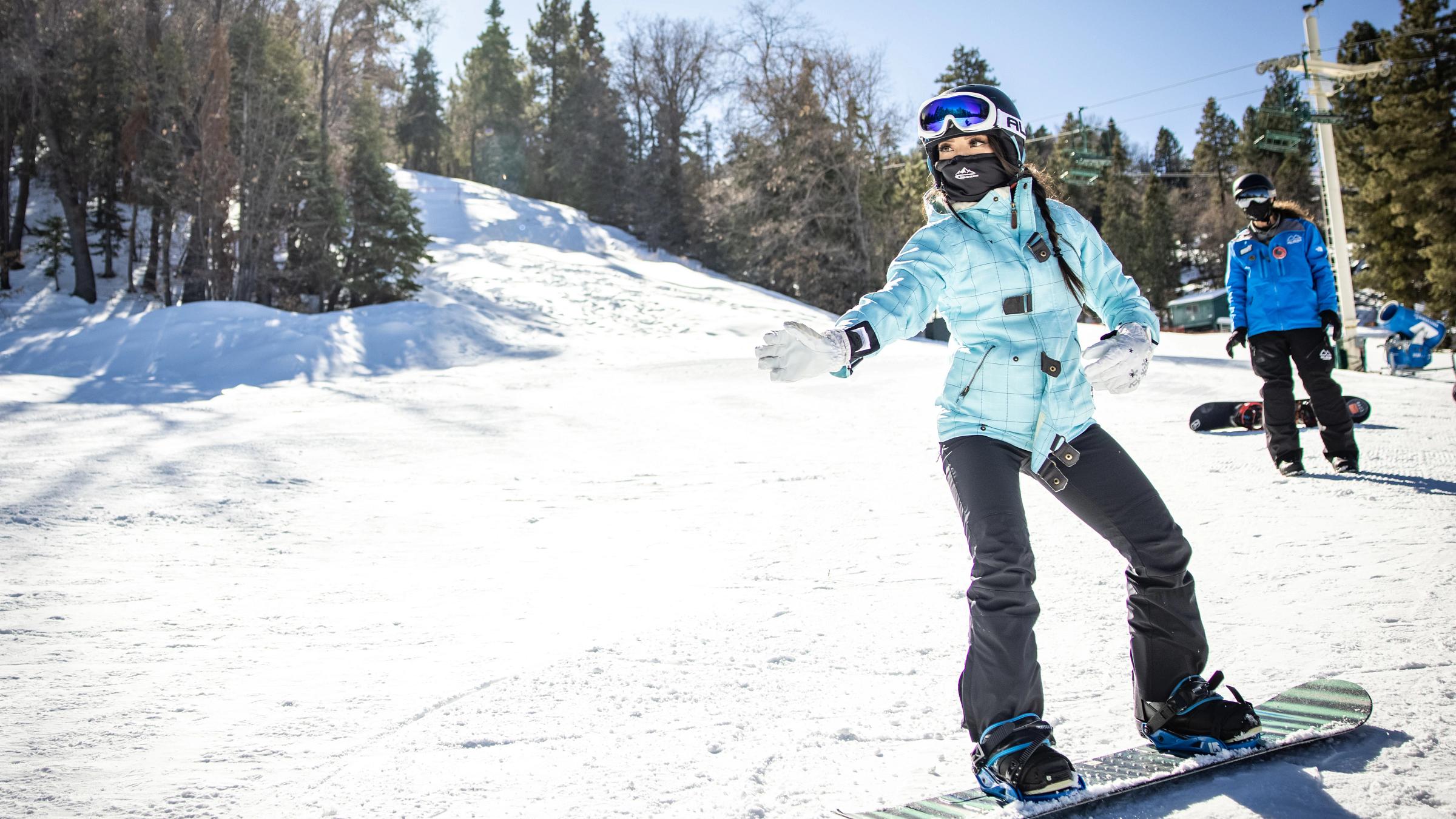 Girl taking a snowboard lesson, raising arm to point in a direction.