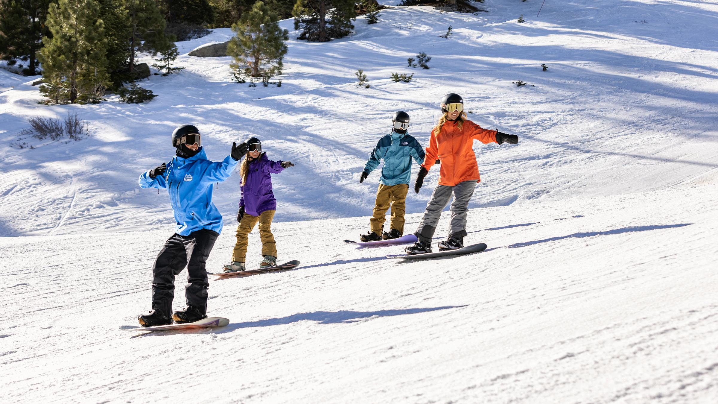 Three snowboarders taking a snowboard lesson