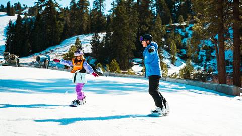 A certified snowboard instructor teaching a kiddo on the beginner hill at Snow Valley during winter
