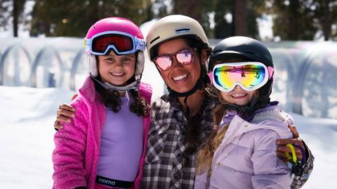 Two kiddos in snow gear and helmets with their instructor during a winter lesson smiling for the camera