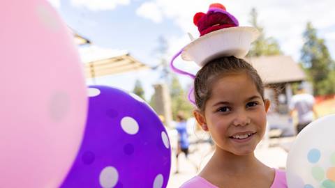Young girl wearing a party hat smiling near balloons