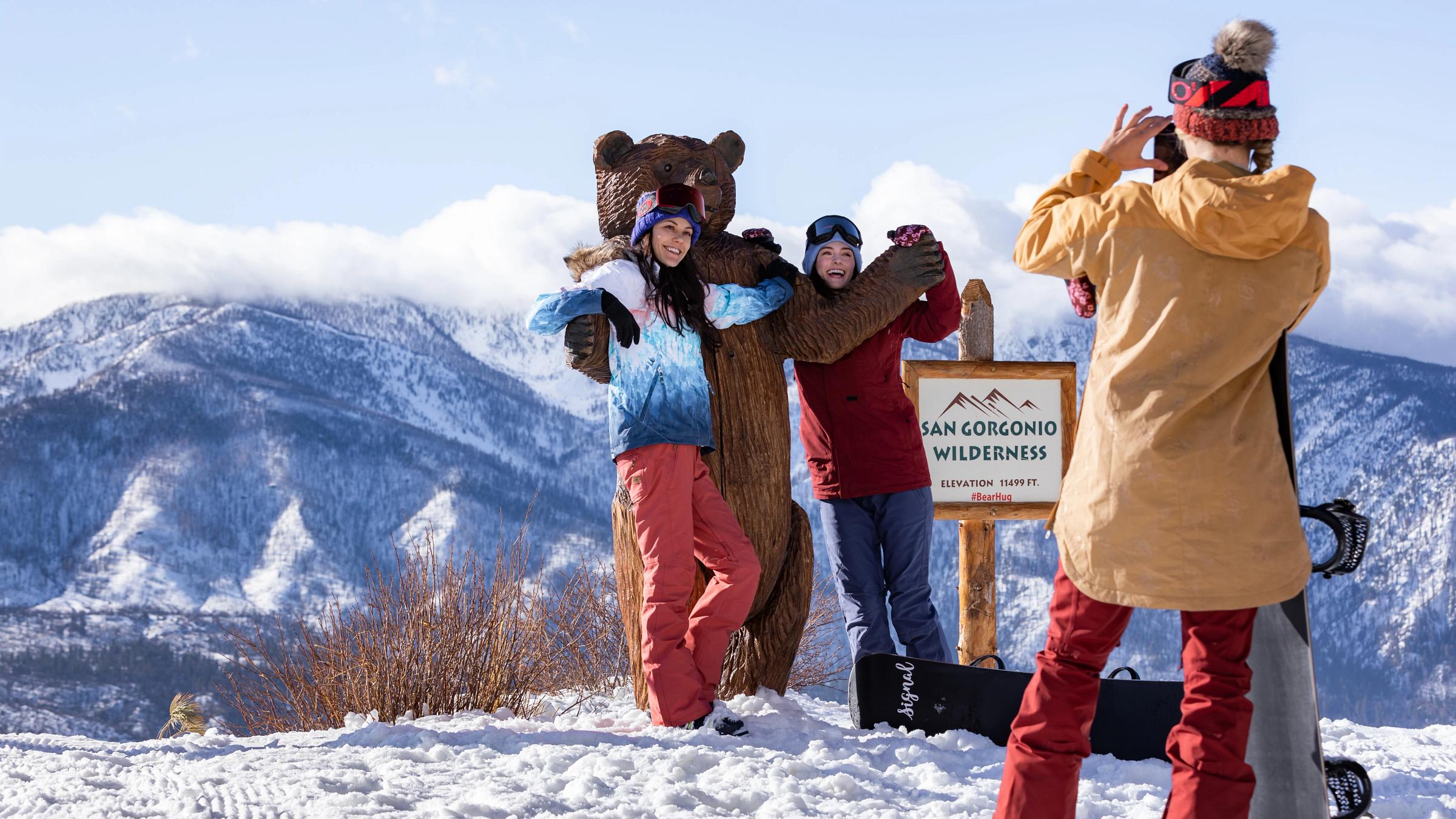 Two girls taking a photo next to a wooden bear