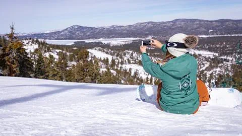 Girl taking a selfie on the top of the snowy mountain in snowboarding gear