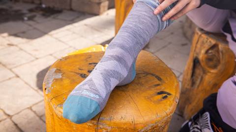 An adult putting on grey and teal Darn Tough winter socks