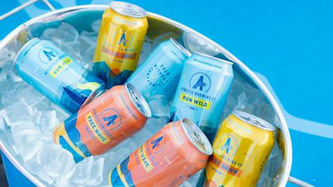 A bucket of ice on a blue table cloth with seven various cans of Athletic Brewing beverages.