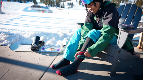 Female snowboarder sitting on a chair in the base area putting on socks