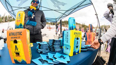 Athletic Brewing activation tent with branded beverages and koozies on a table for guests to take and try out.
