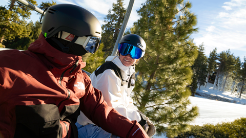 Snowboarders on a chairlift looking at each other smiling