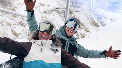 Two snowboarders on the chairlift, smiling at the camera for snow