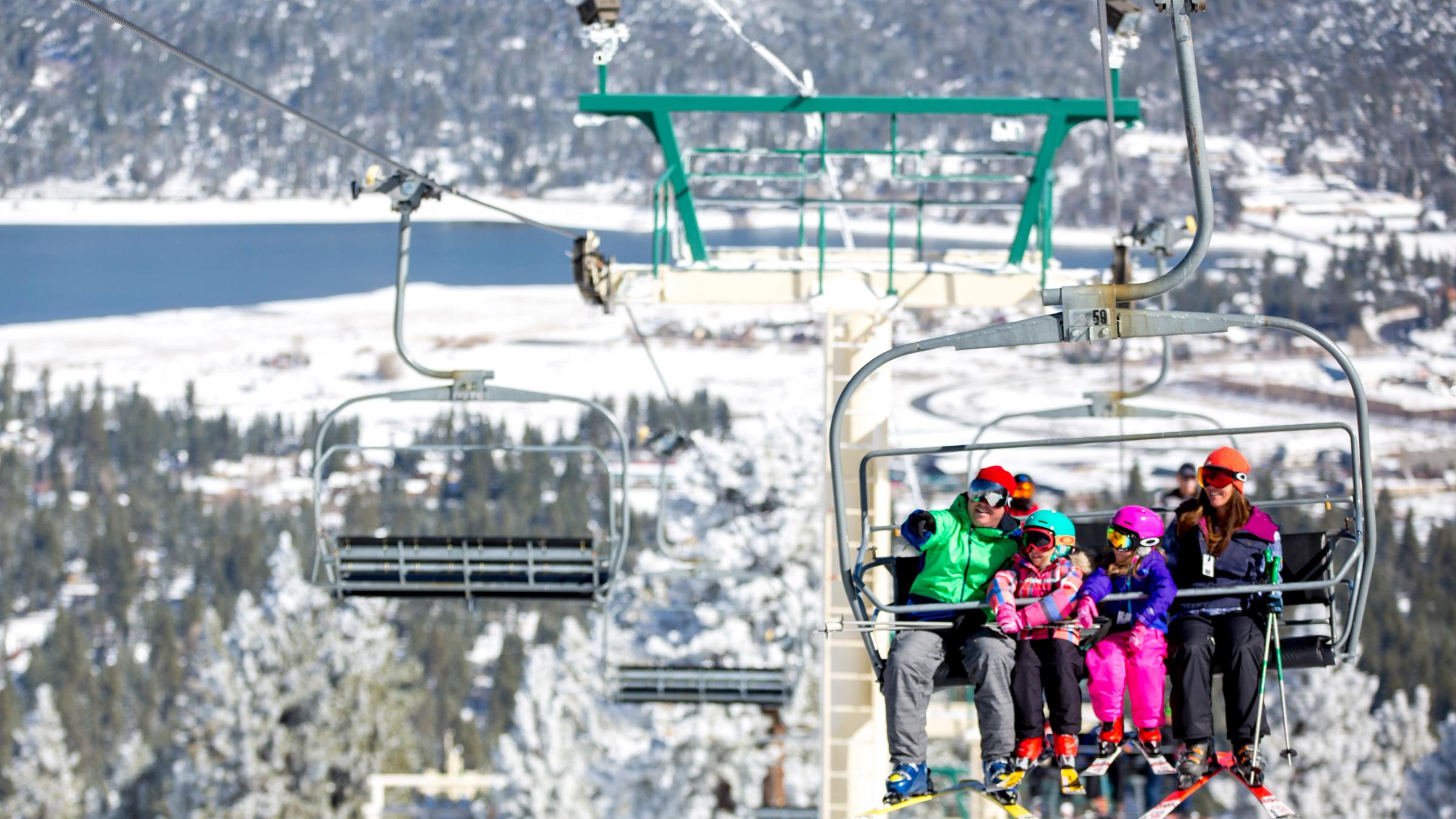 Family on a chairlift with a snowy lake in the background.