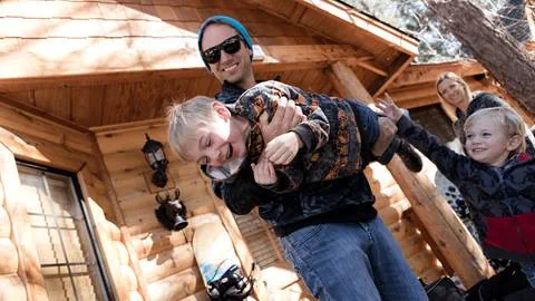 Family of 4 in front of their big bear lake lodging, dad carrying son