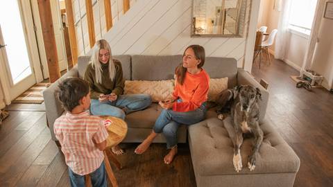 Two people sitting on a couch, one is standing, inside a condo