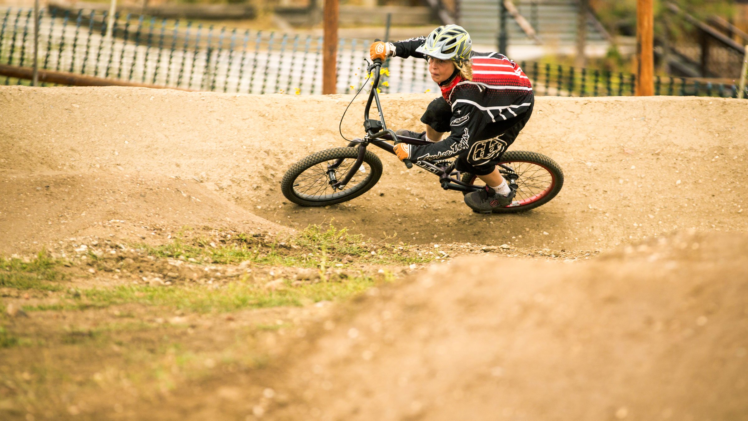 Mountain biker in black pants and a red with black jersey riding through a berm on the course.