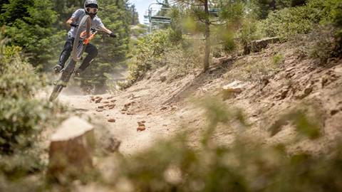 Rider lifting off a jump on an ebike rental at Snow Summit Bike Park, kicking up dust along one of the rugged bike trails.