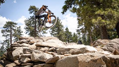 Rider on an ebike rental launching off a rocky feature at Snow Summit Bike Park, riding advanced bike trails through the forest.