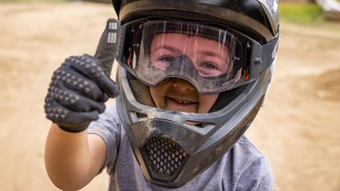 toddler mountain biker giving a thumbs up wearing a full face helmet