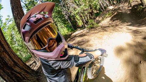 Kid on a mountain bike on a dirt trail wearing a full face helmet with reflected goggles during the summer.