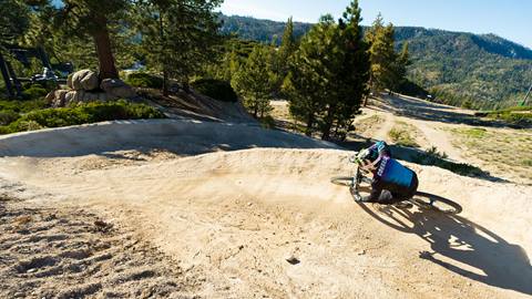 A solo mountain biker riding through a dirt berm at Snow Valley bike park