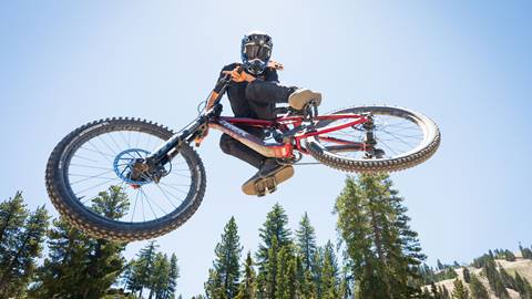 A mountain biker in all black with a full face helmet catching air off at Snow Valley