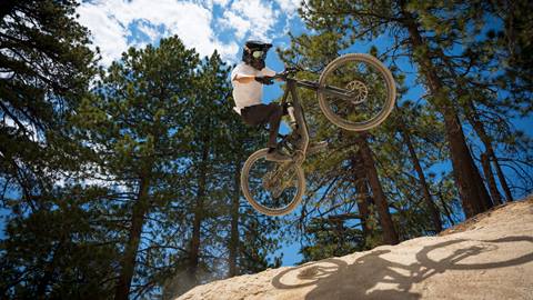 A mountain biker in black pants, a white jersey, black bike and full face helmet catching air off a dirt jump at Snow Valley