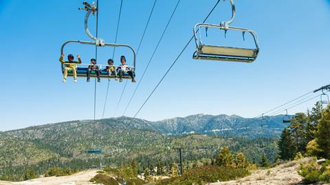 Four mountain bike riders on Snow Valley's Chair 1 during the summer season, on a blue sky day.