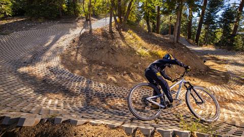 Mountain bike rider in black pants, black long sleeve shirt, and full face helmet riding through a pavement berm at Snow Summit's Bike Park