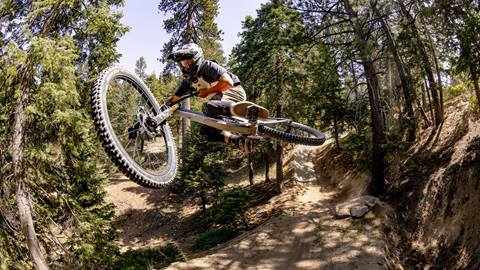 Adult on a mountain bike, wearing a full face helmet, on their bike mid-air after hitting a bike park jump.